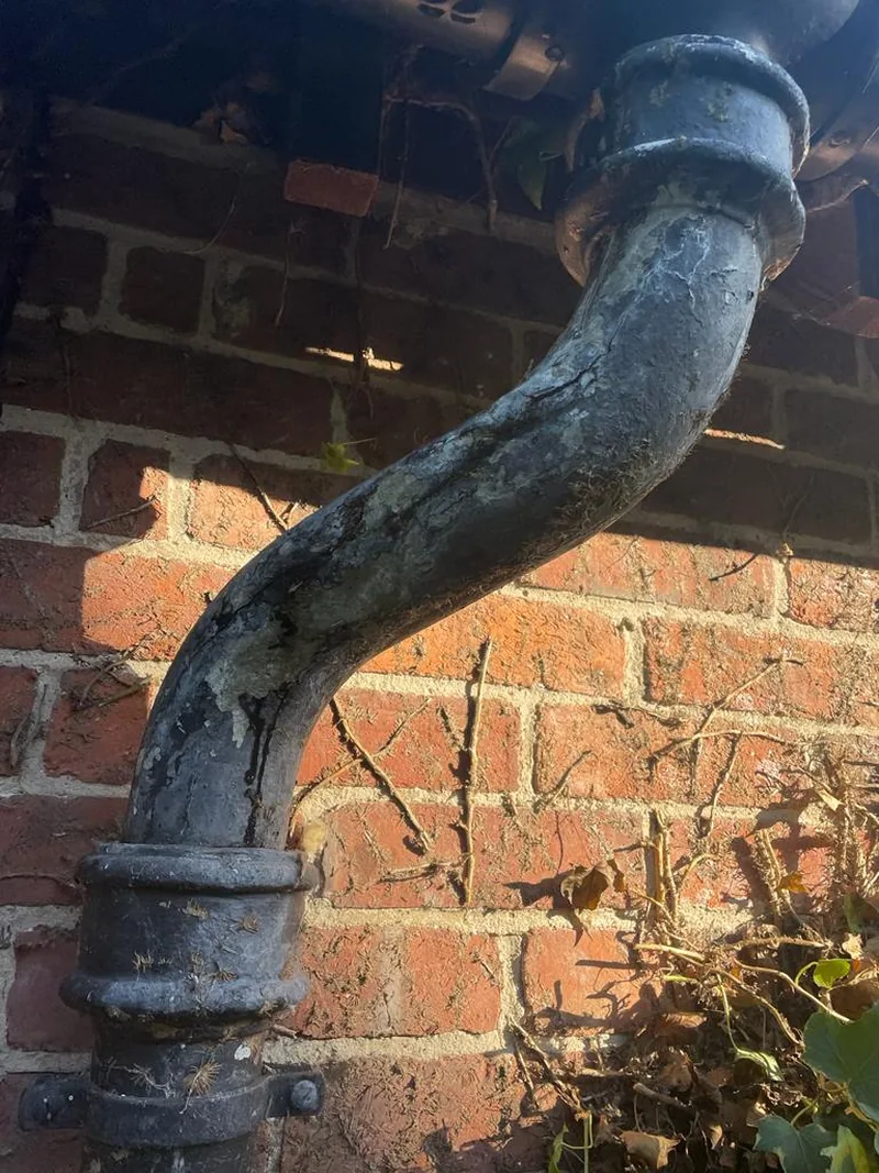 Weathered traditional metal downpipe offset with socketed joints against brickwork