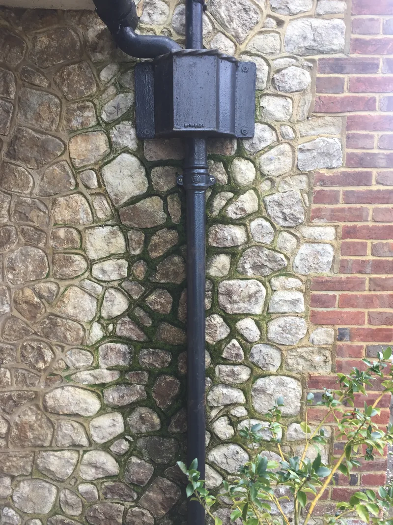 Traditional black rainwater hopper and downpipe against a stone wall