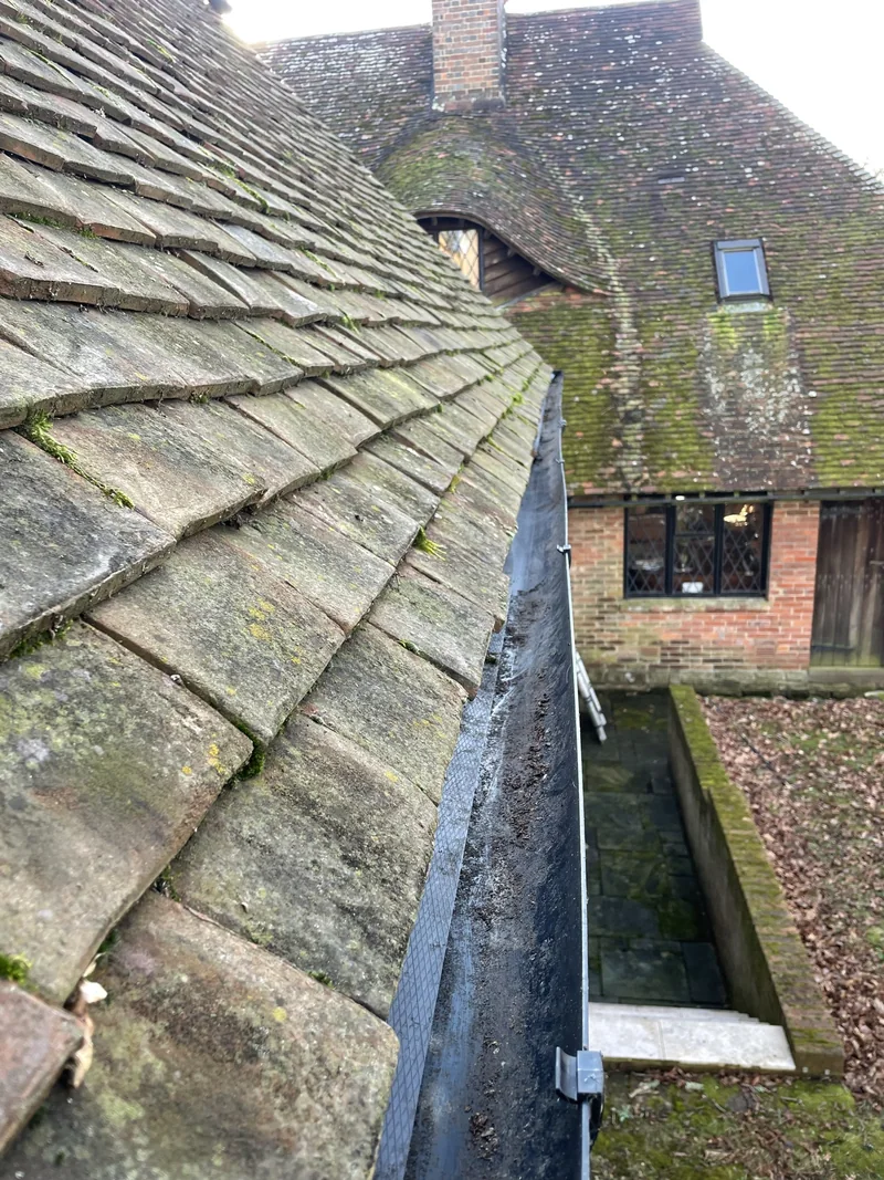Gutter channel alongside a tiled roof with a brick-and-timber elevation beyond