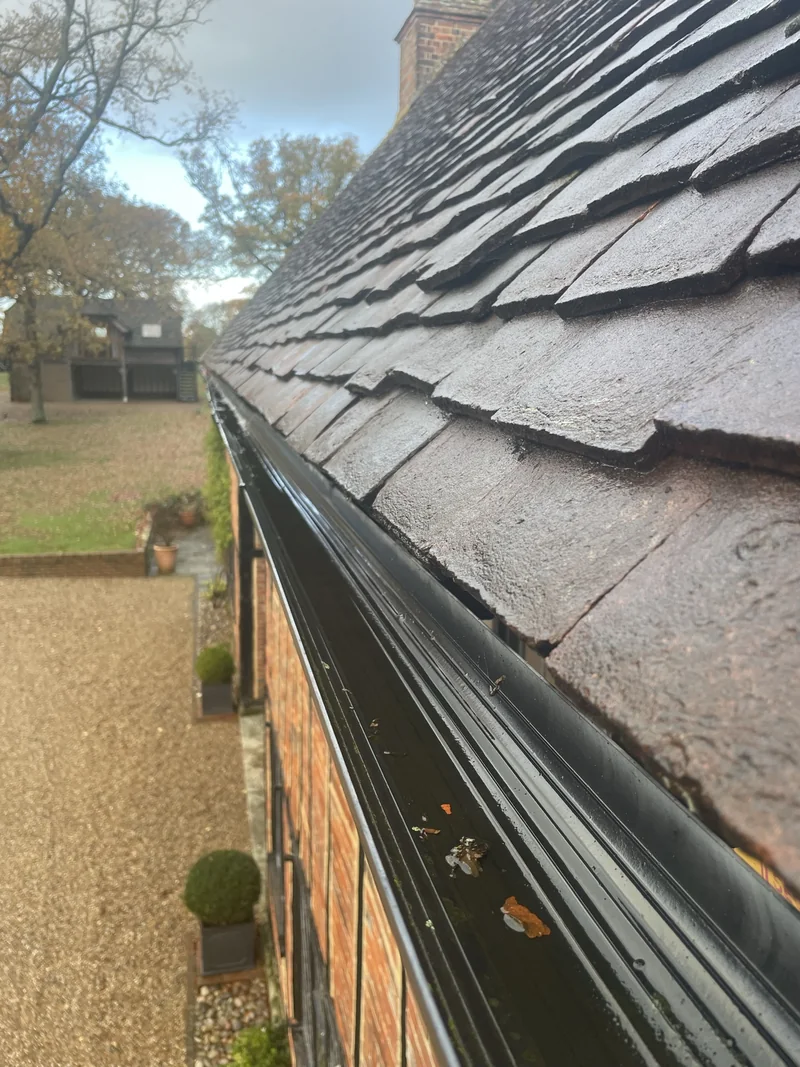 Black gutter beneath a tiled roof with a small amount of visible leaf debris