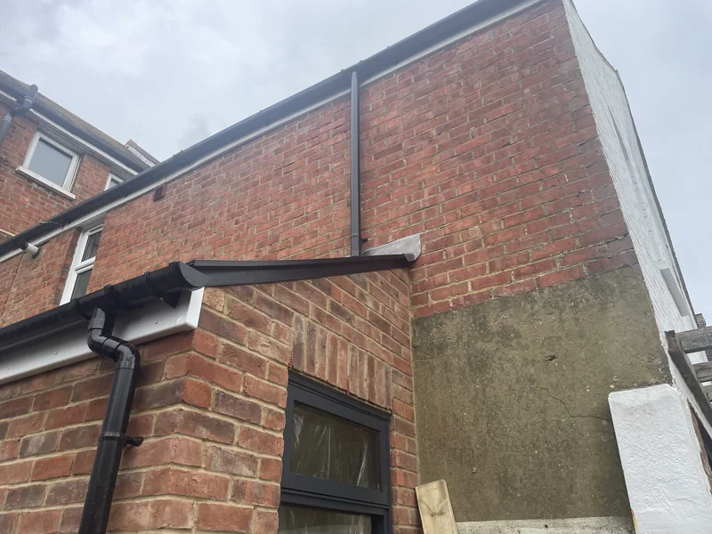 Black guttering and downpipes along the rooflines of a brick extension