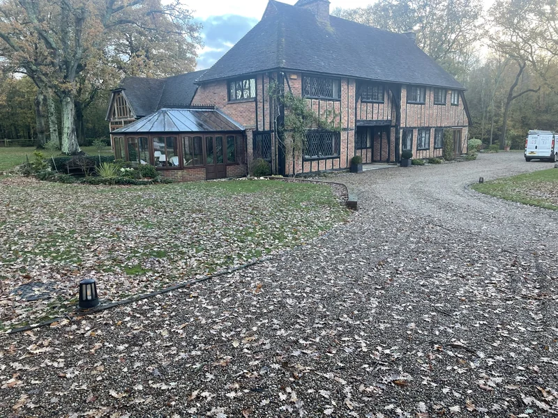 Substantial timber-framed house with a glazed extension, mature trees and a gravel drive