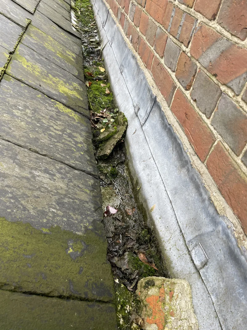 Debris and moss collected in a narrow channel between roof tiles and brickwork