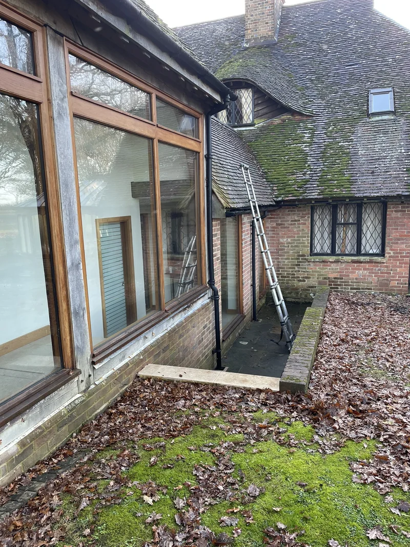 Glazed extension beneath adjoining tiled roof slopes, with a ladder in the narrow space beside it